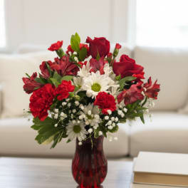 Red roses and white daisies arranged in a red glass vase