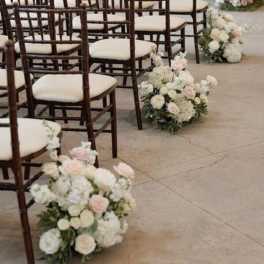 Pastel floral arrangements line rows of chairs in a ceremony space.