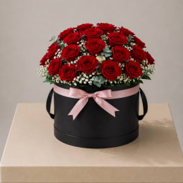 Red roses arranged in a black round box with a pink ribbon