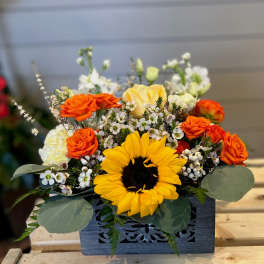 Orange roses and a yellow sunflower in a dark wooden box