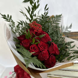 Wrapped bouquet of red roses with greenery and a Happy Valentine’s Day pick, tied with red ribbon.