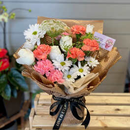 Bouquet of white daisies, roses, and pink carnations wrapped in brown paper
