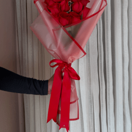 Bouquet of red roses wrapped in pink translucent paper with a red ribbon