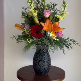 Mixed bouquet in a black vase with lilies, roses, and a red gerbera daisy