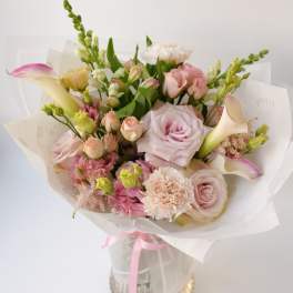 Bouquet of pale pink and white flowers wrapped in white paper with a pink ribbon