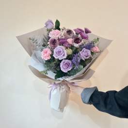 Hand-tied bouquet of lavender roses and pink flowers wrapped in paper
