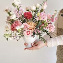 Handheld bouquet of pink, white, and peach flowers in a white vase