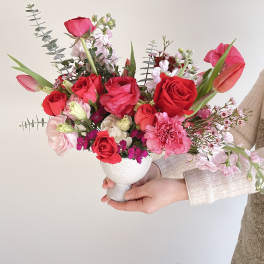 Handheld bouquet of red and pink flowers in a white vase