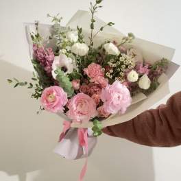 Handheld bouquet of pink and white flowers wrapped in paper