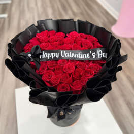 Bouquet of red roses wrapped in black paper with a Valentine’s Day ribbon