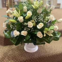 White roses and lilies arranged in a white pedestal vase