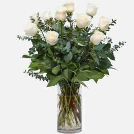 White roses in a clear glass vase with eucalyptus greenery