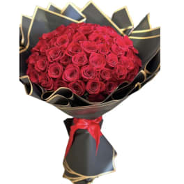 Bouquet of red roses wrapped in black paper with gold trim and a red ribbon