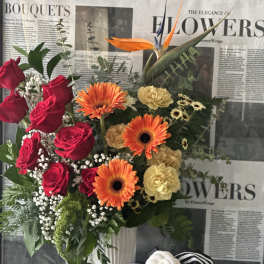 Bouquet of red roses, orange gerberas, and pale carnations in a white vase