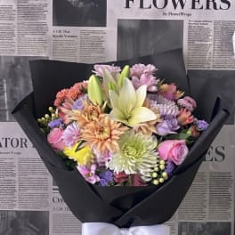 Mixed pastel bouquet with lilies, roses, and chrysanthemums wrapped in black paper