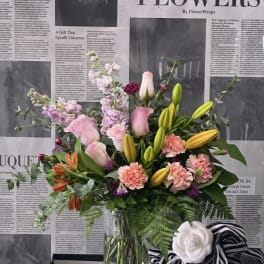 Mixed bouquet with pink roses, lilies, carnations, and purple blooms in a glass vase