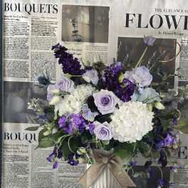 Lavender and white bouquet in a white vase with a burlap bow