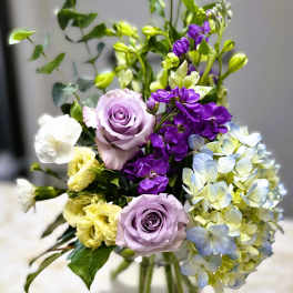 Lavender roses with purple and pale blue flowers in a glass vase