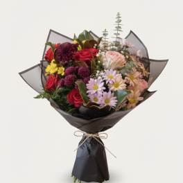 Bouquet of mixed flowers wrapped in dark paper with a bow