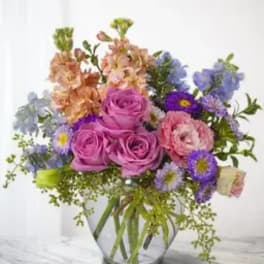Mixed bouquet of pink roses and purple flowers in a clear glass vase