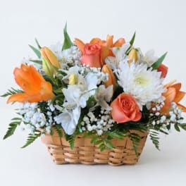 Basket arrangement of orange roses, white flowers, and lilies