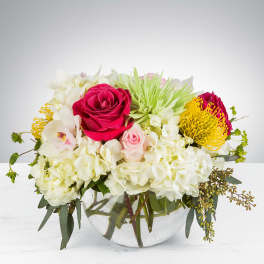 Mixed bouquet of roses, hydrangeas, and white blooms in a glass bowl vase