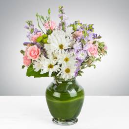 Mixed bouquet of white daisies, pink carnations, and lavender flowers in a green glass vase