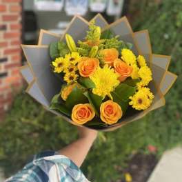Bouquet of orange roses and yellow flowers wrapped in gray paper