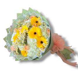Bouquet of yellow gerbera daisies, peach roses, and white flowers wrapped in green paper