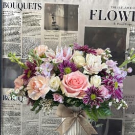 Pink and purple mixed bouquet in a white vase with a burlap bow