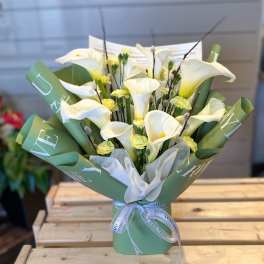 Bouquet of white calla lilies and small yellow flowers in green wrap
