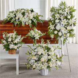 White funeral floral arrangements with lilies and roses around a casket