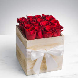 Red roses arranged in a square wooden box with a white ribbon