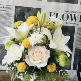White lilies and yellow pompons arranged in a white vase with a pale rose center
