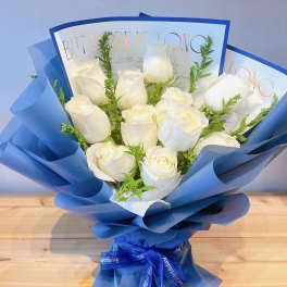 Bouquet of white roses wrapped in blue paper with a ribbon