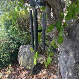 Black wind chimes hanging from a tree branch in a garden