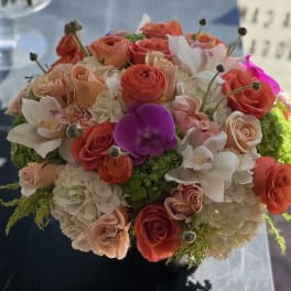 Round bouquet of coral and white flowers with a purple orchid accent