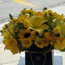Yellow floral arrangement in a black handbag-style container