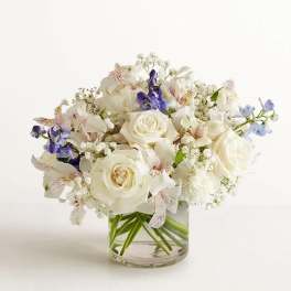 White rose bouquet with purple and pale blue flowers in a clear glass vase