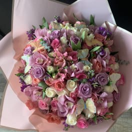 Large pink bouquet of roses and orchids wrapped in blush paper