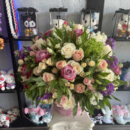 Large bouquet of pink, cream, and purple roses in a pink container