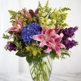 Bouquet of pink lilies, blue hydrangea, and purple flowers in a clear vase