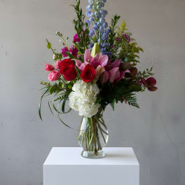 Mixed bouquet with roses, lilies, hydrangea, and blue delphinium in a glass vase