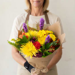 Bouquet of yellow, purple, and red flowers wrapped in brown paper