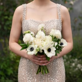 Woman holding a white bridal bouquet with dark-centered anemones