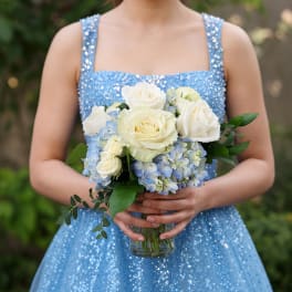 Woman in a blue dress holding a bouquet of white roses and blue hydrangeas in a glass vase