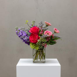 Mixed bouquet of pink roses, purple flowers, and gerbera daisies in a glass vase
