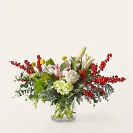 Arrangement of white lilies, roses, and red berry branches in a glass vase