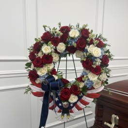Red and white rose funeral wreath on a stand with a patriotic ribbon