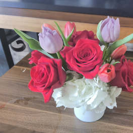Short arrangement of red roses, tulips, and white hydrangeas in a white vase
